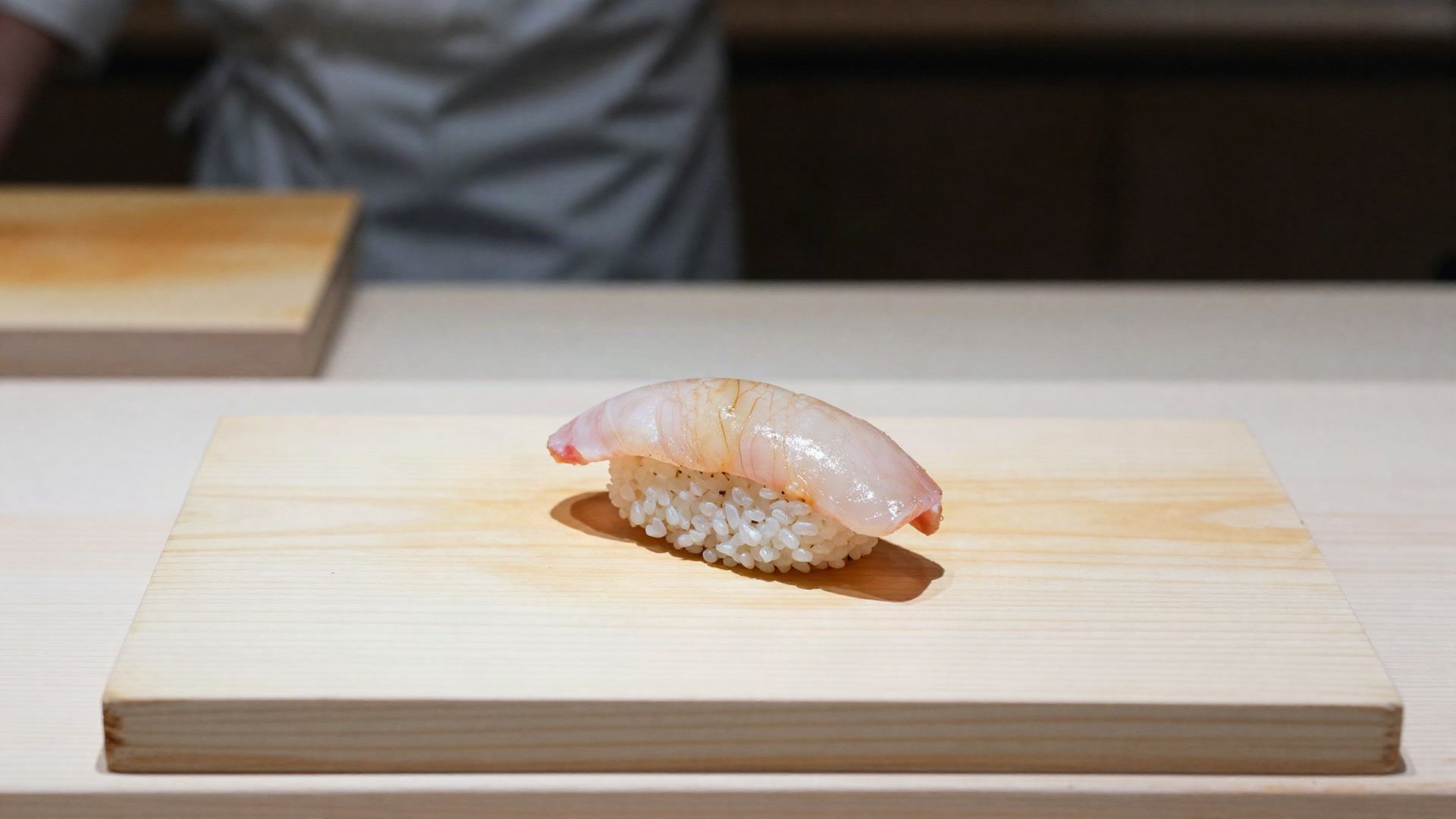 A single piece of nigiri resting on a pale cypress board at the Nagi counter